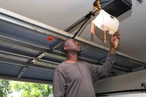 Technician inspecting a ceiling-mounted garage door opener inside a garage