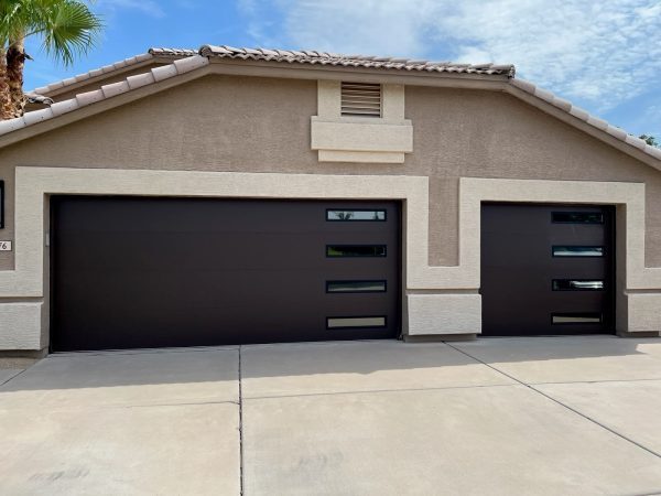 Three dark, modern garage doors with rectangular windows installed on a beige stucco home.