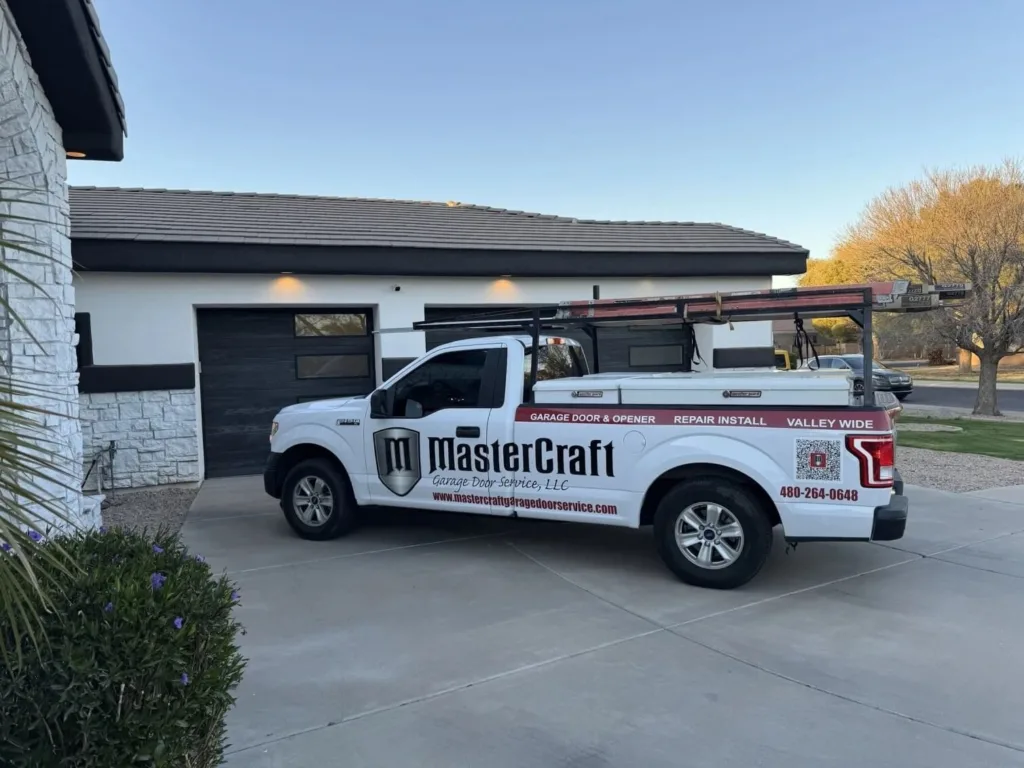 White Ford pickup truck for MasterCraft Garage Door Service parked in front of a modern home with black garage doors.